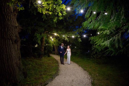 bride and groom walking by the lake with fairylight above them at manor by the lake