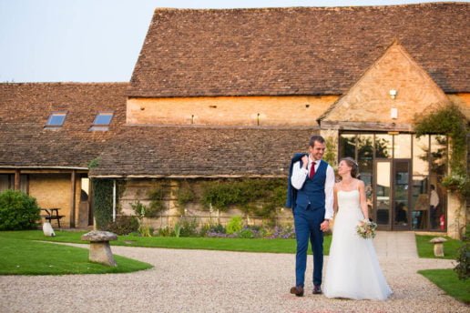 wedding couple walking holding hands with the great tythe barn behind them