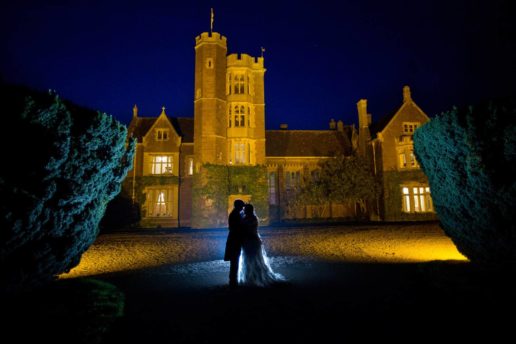 night shot of a wedding couple kissing each other backlit with st audries park lit up by lights