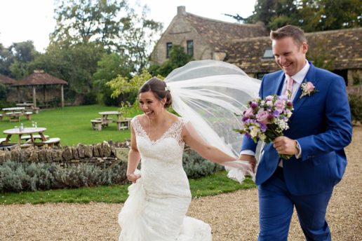 couple running away from rain holding hands at the great tythe barn tetbury