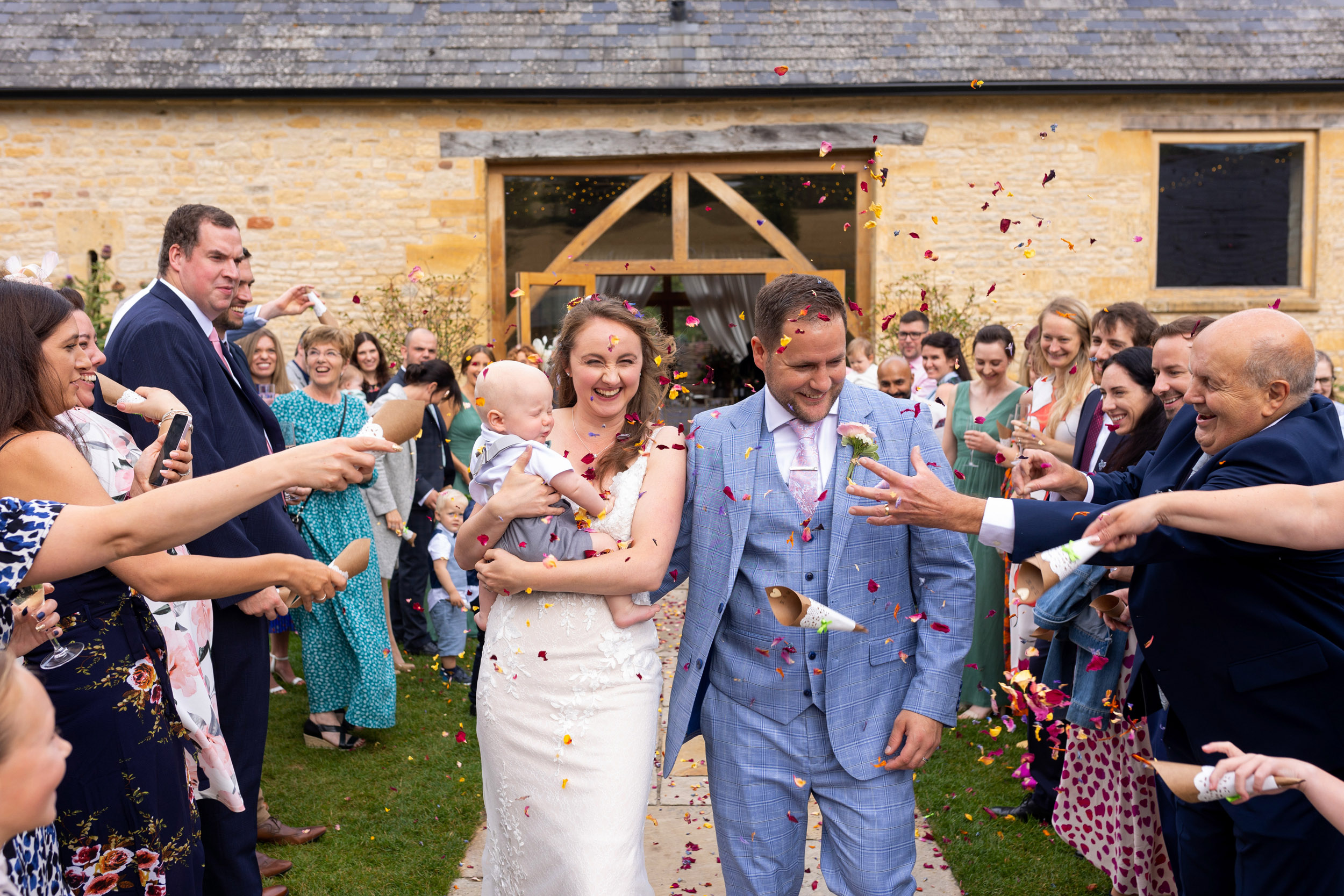 bride and groom walking through confetti arch at barn at upcote cotswolds