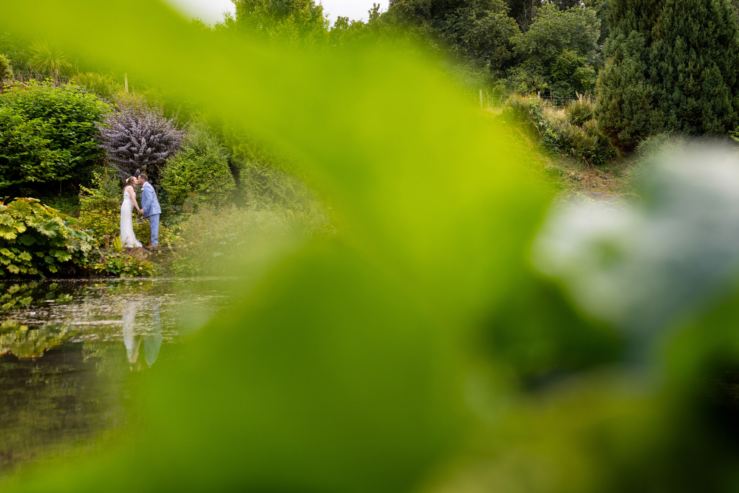 bride and groom kissing by the pond at barn at upcote cotswolds