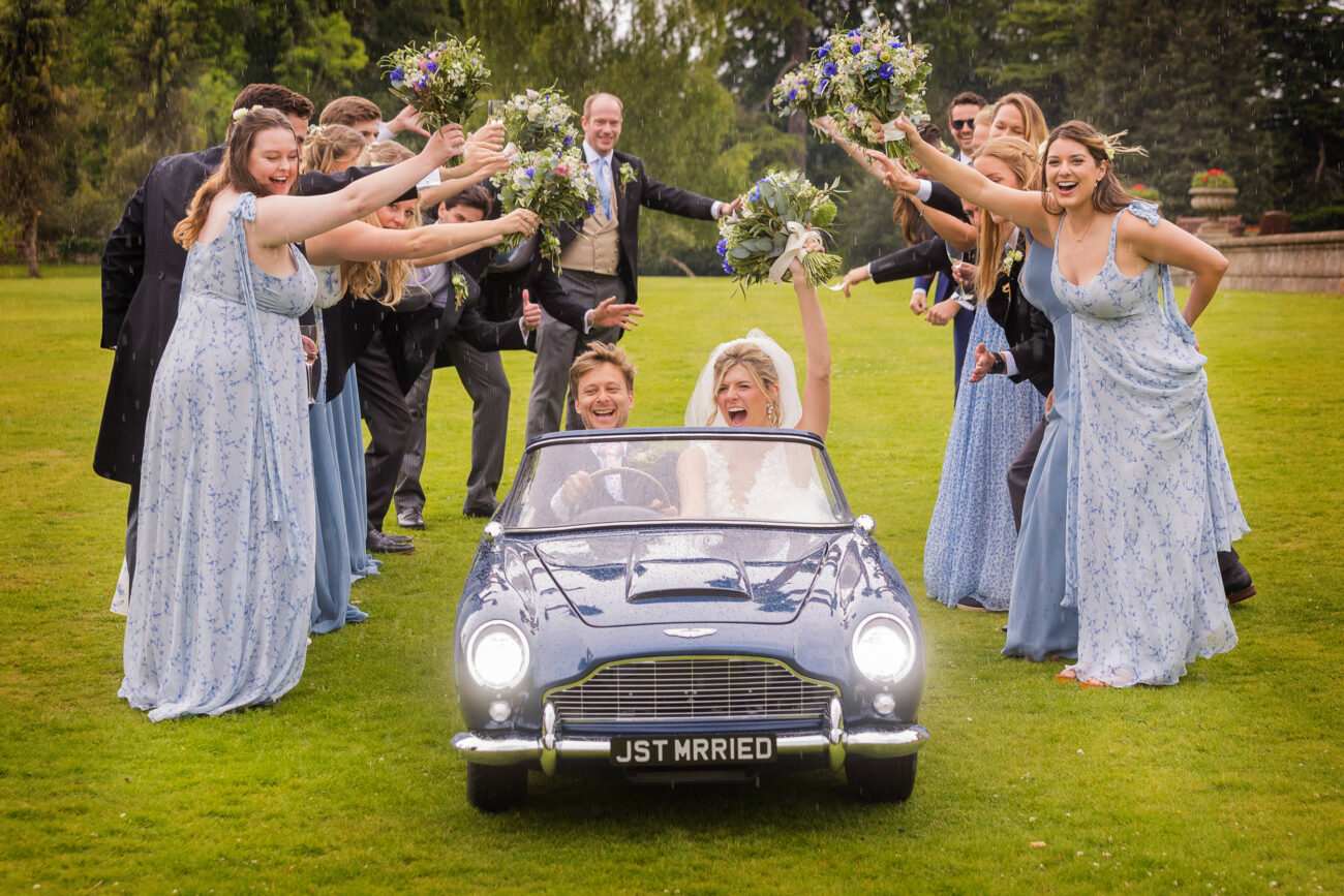 bride and groom driving little car through the arc made by bridesmaids and groomsmen