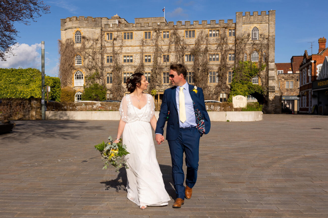 wedding couple walking holding hands with taunton castle hotel behind