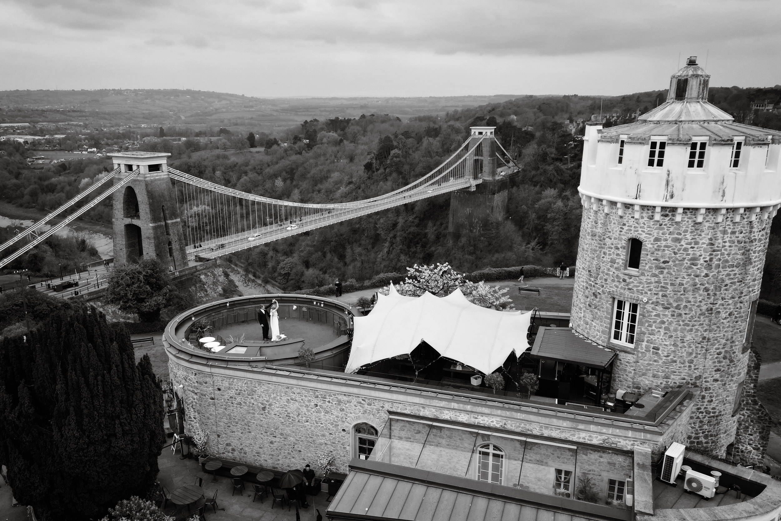 AERIAL SHOT OF BRIDE AND GROOM DANCING AT CLIFTON OBSERVATORY TERRACE WITH CLIFTON SUSPENSION BRIDGE IN THE BACKGROUND. CLIFTON OBSERVATORY WEDDING PHOTOGRAPHY